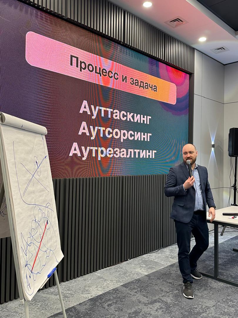 Алексей Беба с микрофоном у экрана со слайдом «Процесс и задача»